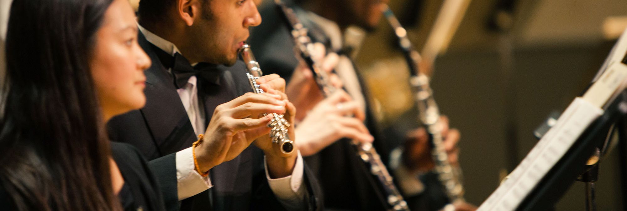 A performer wearing a tuxedo plays the flue in an orchestra