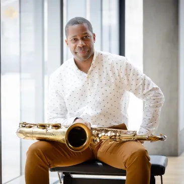 Jason Hainsworth with his saxophone, sitting in a chair