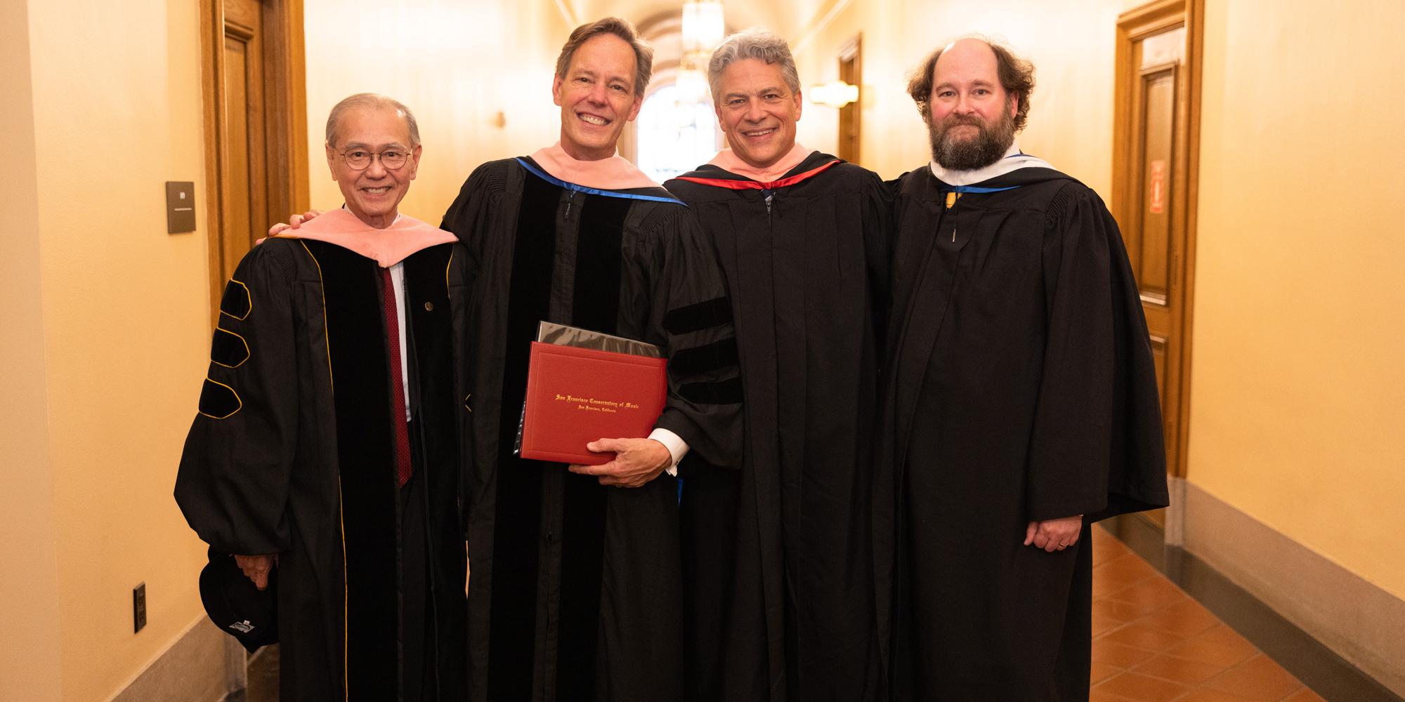 four adults stand in regalia 