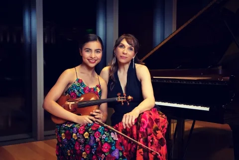 Lara Downes sits at a piano bench with amaryn