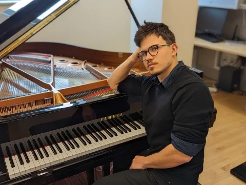 a student looks back at the camera while leaning on the piano casually