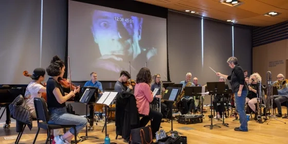 Students rehearse with a movie backdrop playing behind them