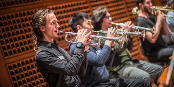 A trumpet player in focus against a backdrop of various other out of focus trumpet players