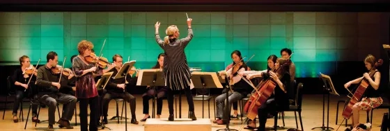 conductor conducting new music ensemble with dramatic hall lighting